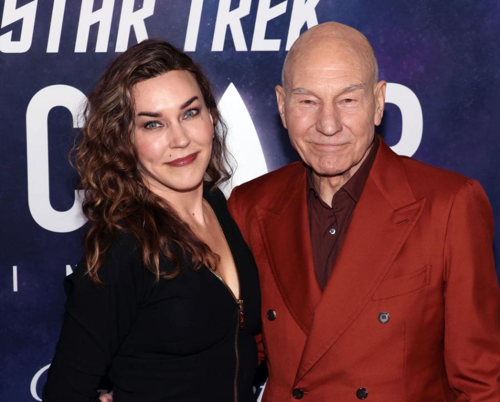 Sunny Ozell and Sir Patrick Stewart attend the Los Angeles premiere of the third and final season of Paramount+'s original series "Star Trek: Picard" both smiling, with sunny wearing black and stewart wearing a red double-breasted jacket.