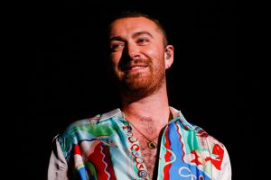Sam Smith smiling looking up to the left wearing a colorful collared shirt.